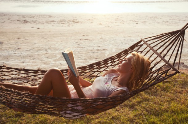 woman reading book in hammock on the beach