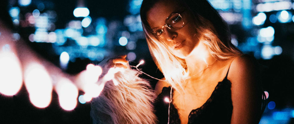 young woman wearing glassess holds string of lights on a summer night