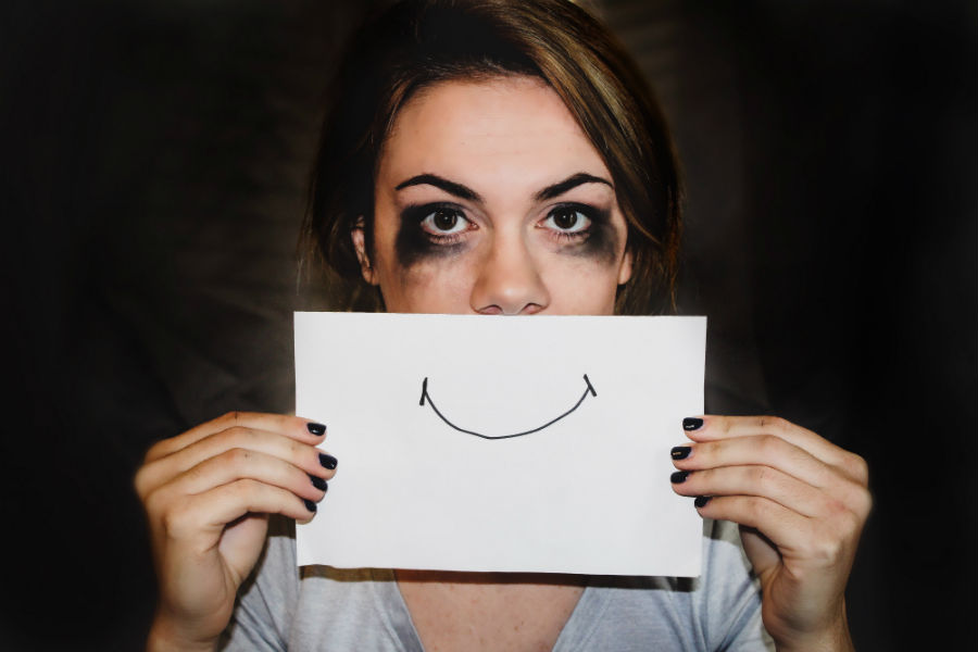 woman with mascara around eyes holding sheet over mouth with drawn on smile